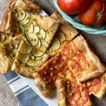 ZUCCHINI and tomato TART, rectangle pieces of tart piled on a white platter. Some tarts are made with tomatoes and some zucchinis.