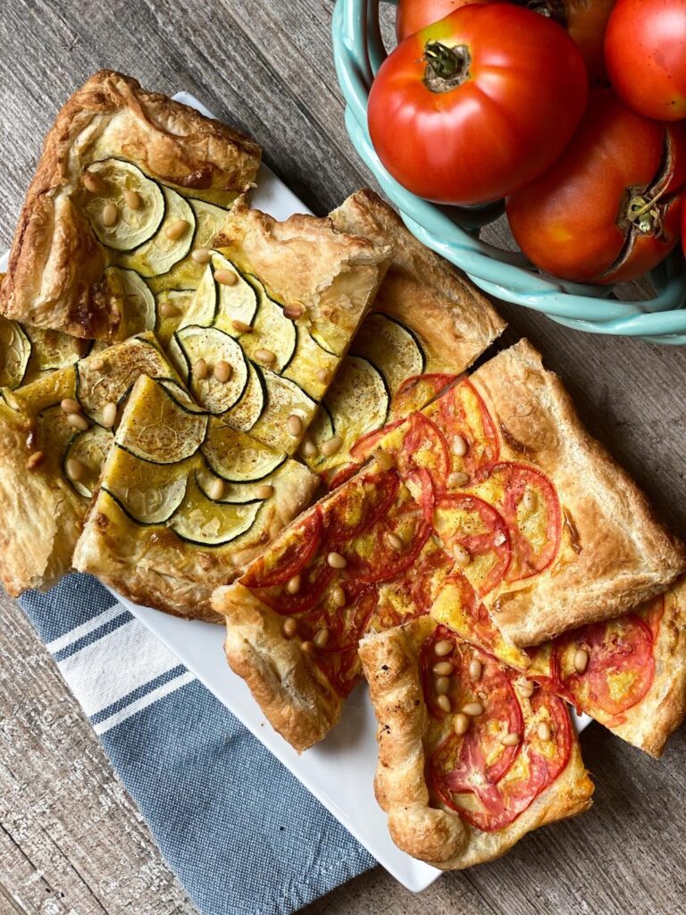 ZUCCHINI and tomato TART, rectangle pieces of tart piled on a white platter. Some tarts are made with tomatoes and some zucchinis.