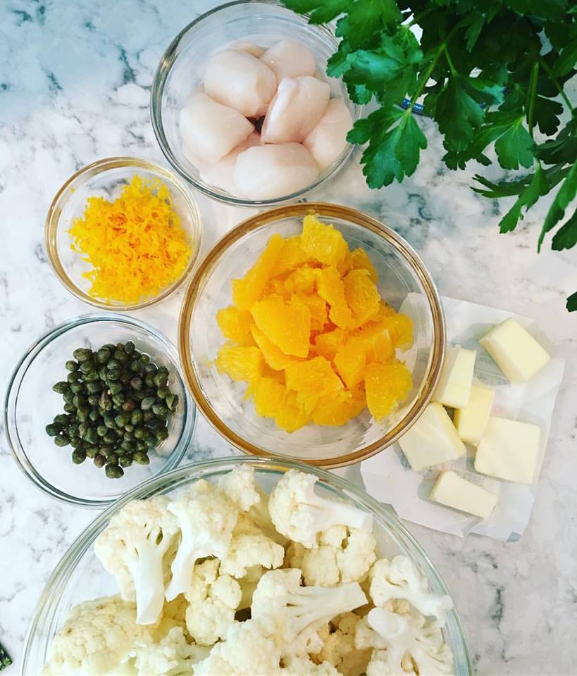 Ingredients for scallops. Orange zet and orange segments, butter, capers, cauliflower and large scallops. Everything is in it's own round bowl.