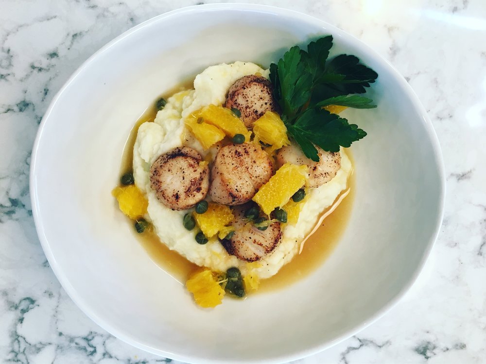five Sea Scallops over top mashed cauliflower with orange segments and capers. garnished with parsley.