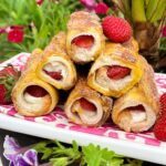 French Toast Roll Ups stuffed with cream cheese and strawberries on a pink napkin and white plate.
