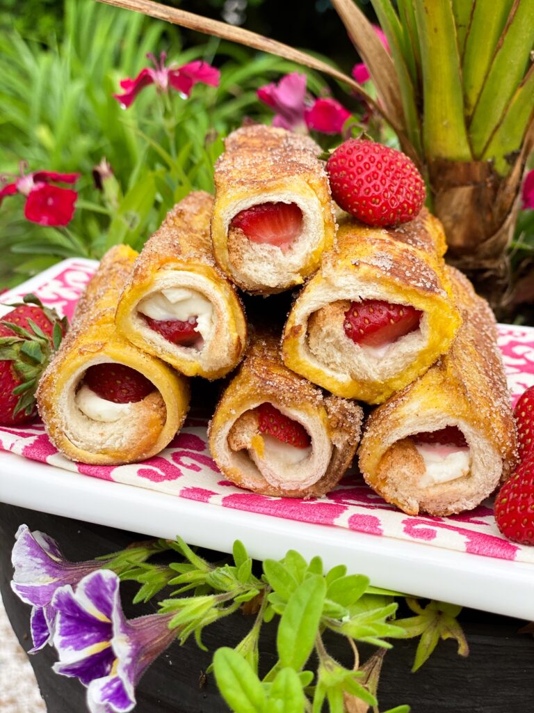 French Toast Roll Ups stuffed with cream cheese and strawberries on a pink napkin and white plate.