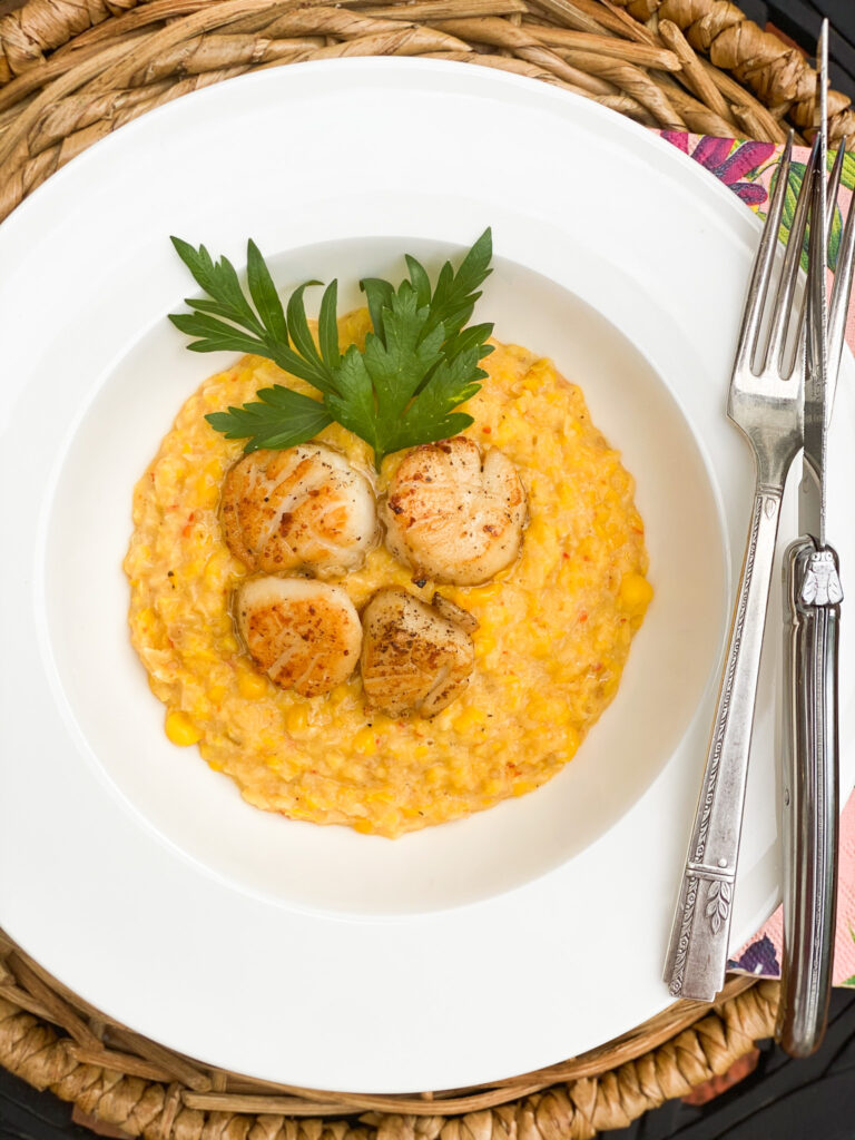 Creamed corn in a round bowl with crispy scallops placed int eh middle with a green garnish of parsley.