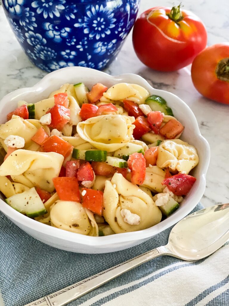 Round bowl full to the top with TORTELLINI PASTA, tomatoes, cucumbers and feta cheese.