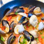 CLAMS-AND-MUSCLES in a staub skillet with tomatoes and red onions. Garnished with fresh parsley.