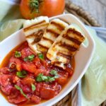 in a small white bowl the roasted tomatoes are filled to the top and sprinkled with fresh basil. To the side are three slices of grilled hallloumi.