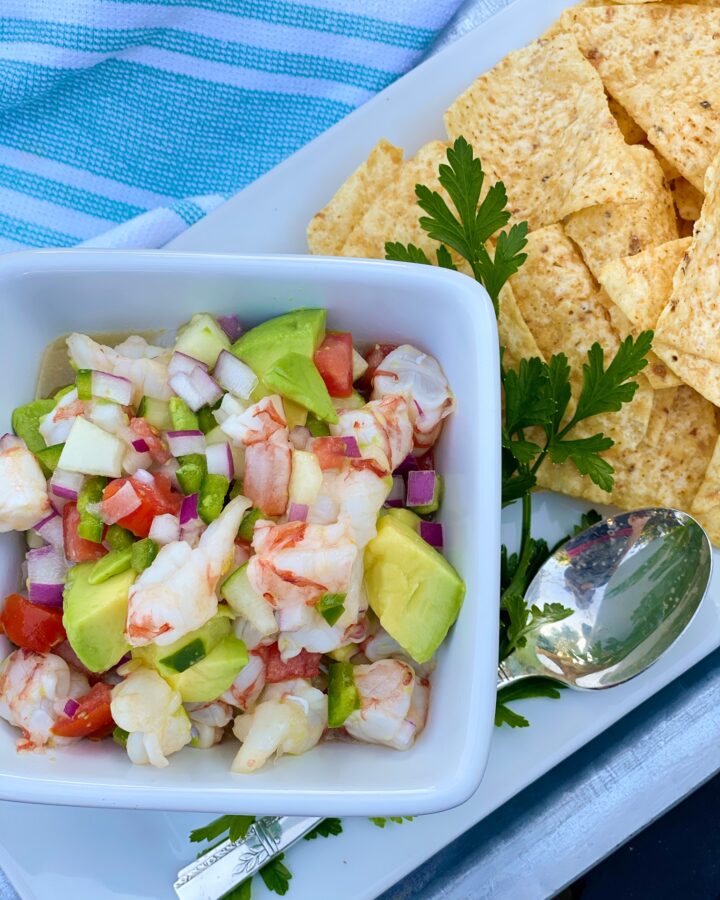 SHRIMP-CEVICHE in a square bowl with silver spoon and a side of tortilla chips.