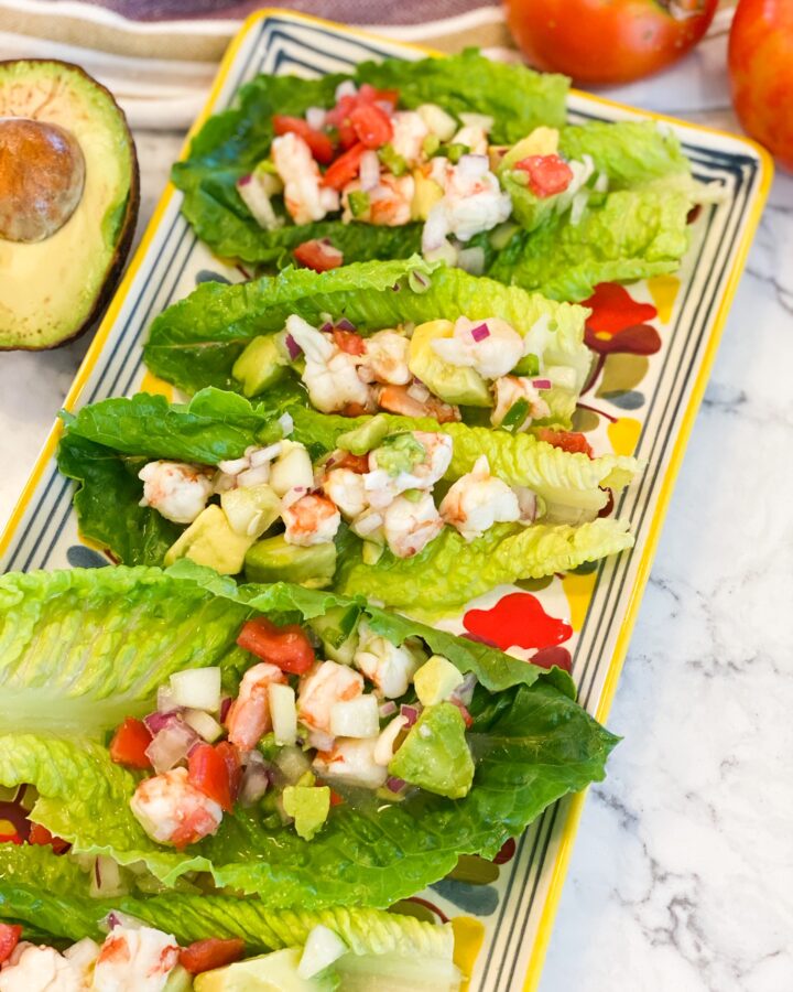 SHRIMP-CEVICHE loaded in to romaine LETTUCE-BOATS. Lettuce boats are lined up on a colorful rectangle platter.