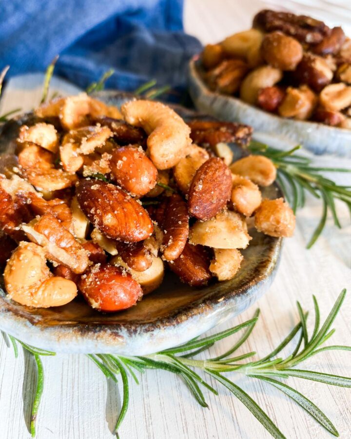 Mixed nuts in small blue bowls on a white tray garnished with fresh rosemary