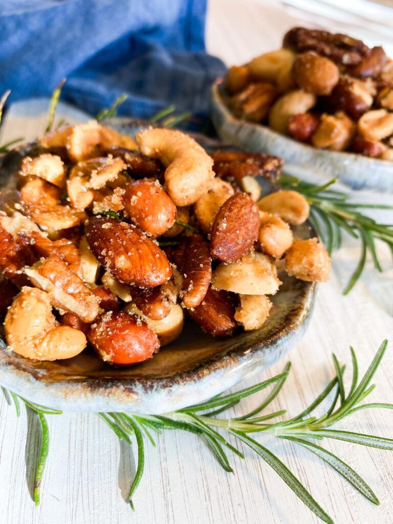 Mixed nuts in small blue bowls on a white tray garnished with fresh rosemary