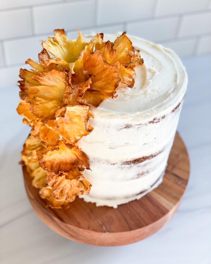 hummingbird cake with white icing and yellow flowers made from dried pineapples