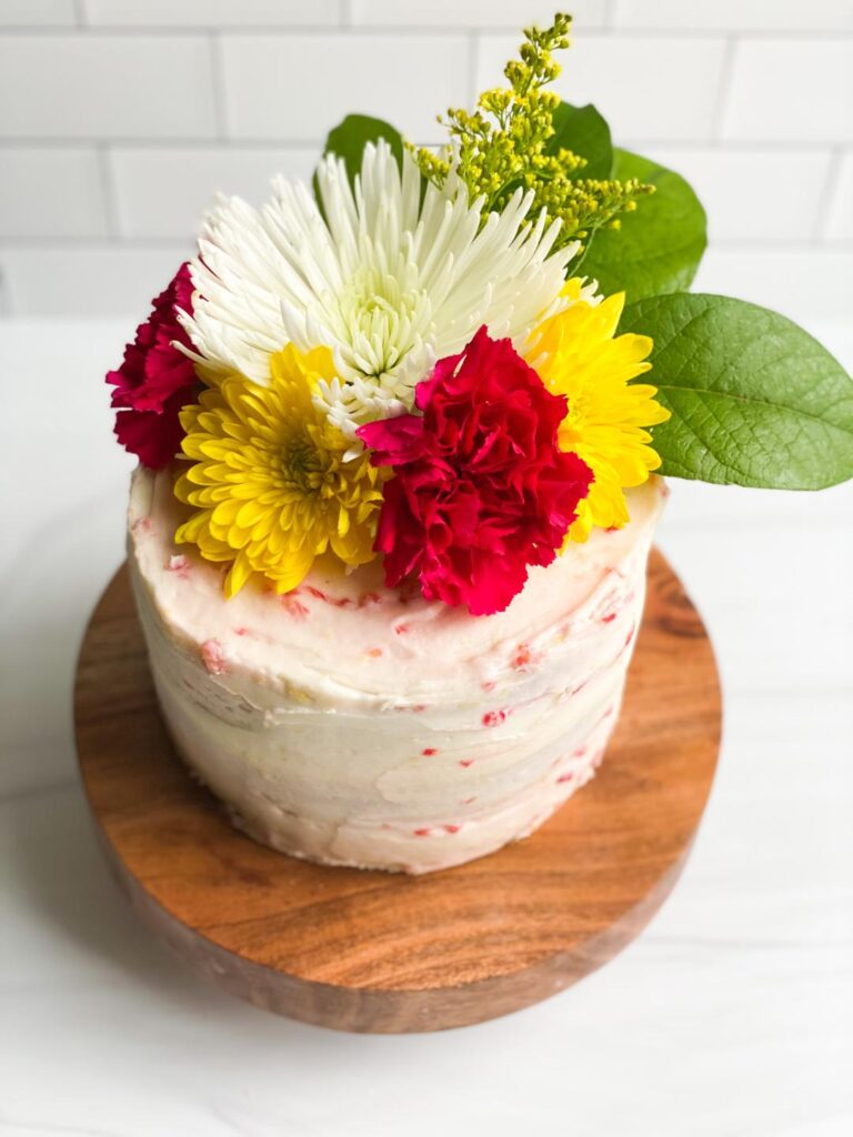 3 layer cake with white icing topped with pink and yellow carnations.