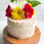 3 layer cake with white icing topped with pink and yellow carnations.